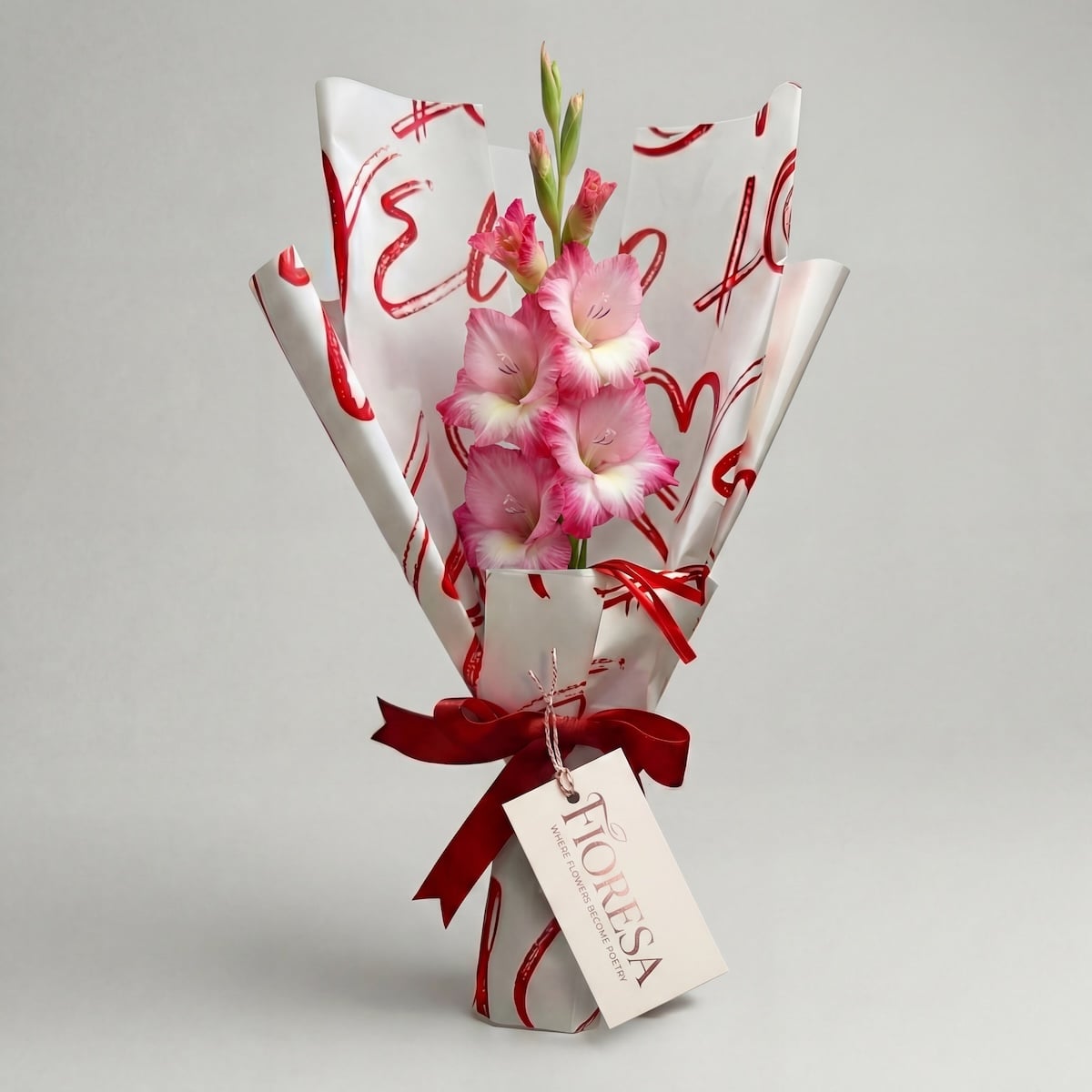 Pink and white gladiolus flowers in a Fioresa heart-patterned gift wrap with a branded tag and red ribbon.
