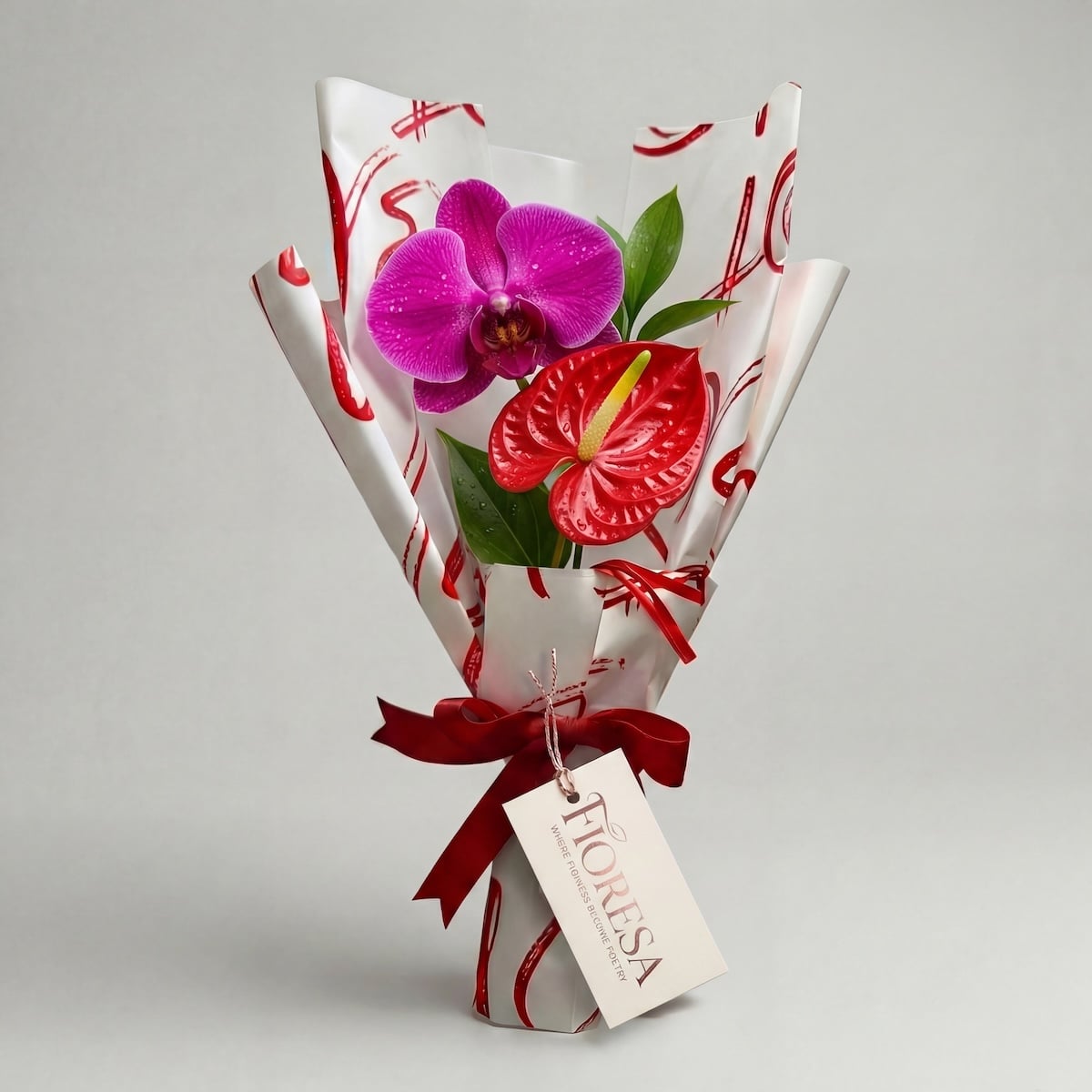 A vibrant purple orchid and a red anthurium bloom in a Fioresa heart-patterned gift wrap with a red ribbon and branded tag on a white background.