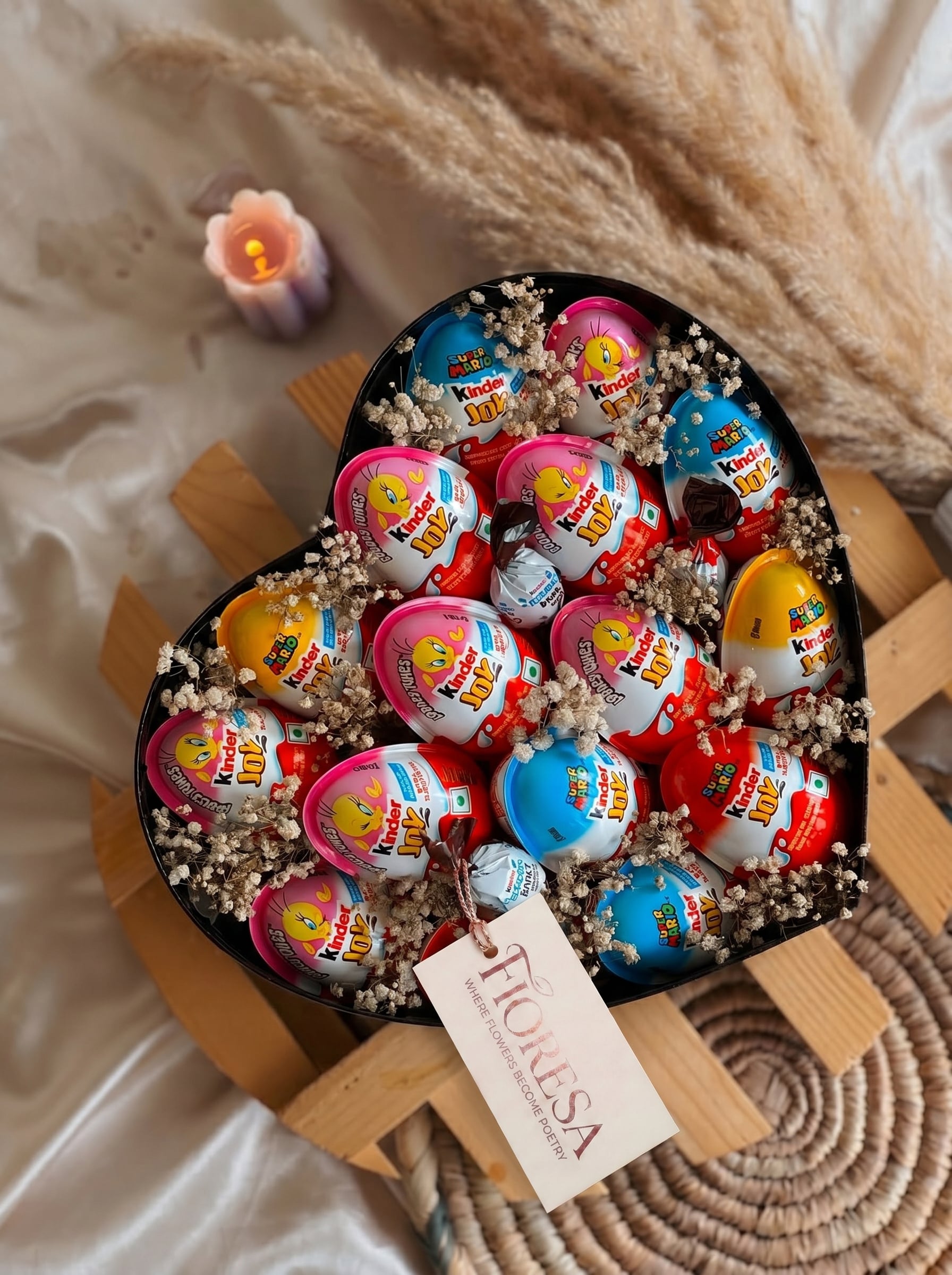 Overhead view of a Fioresa heart box hamper packed with mixed Kinder Joy eggs, pralines and dried baby's breath.