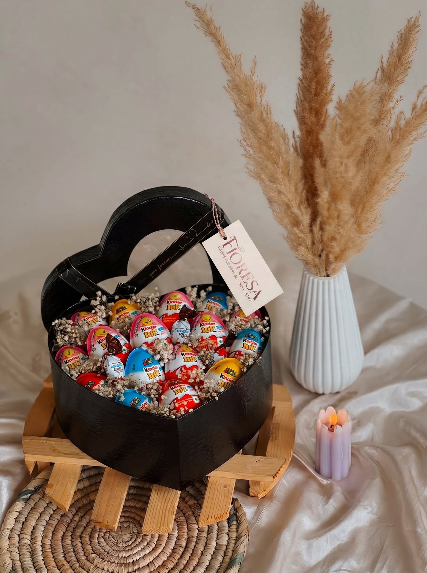 Fioresa Kinder Joy and Ferrero Rocher heart box chocolate hamper with gift tag, styled with pampas grass and a candle.