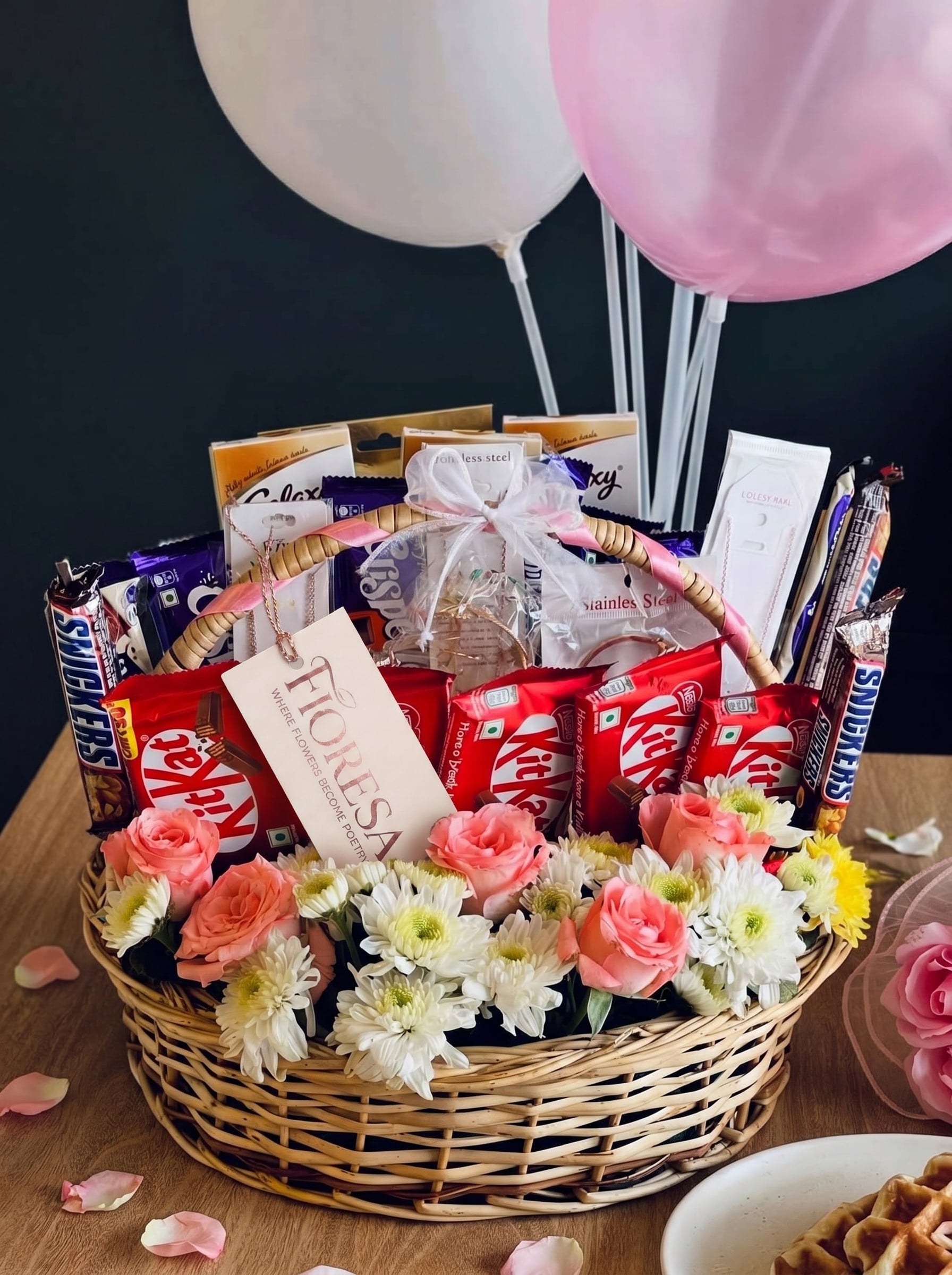 A Fioresa gift basket filled with assorted chocolates, pink roses, and decorated with balloons.